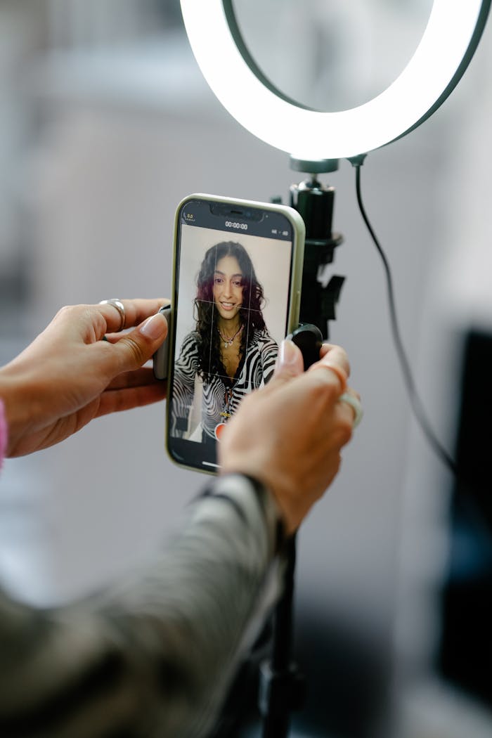 A woman using a smartphone with a ring light for video recording indoors.