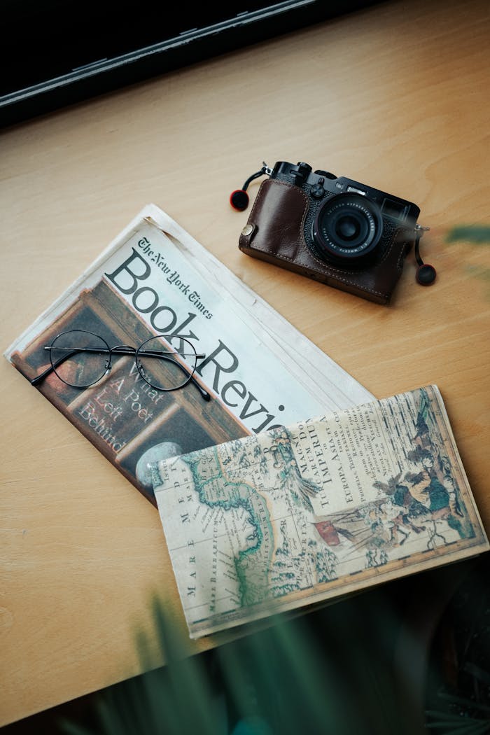 Top view of a vintage camera, newspaper, map, and glasses on a wooden table, perfect for retro and travel themes.