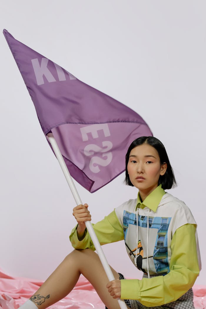 A young woman holding a purple flag with text in a studio setting.